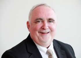 Head and shoulders shot of Jeff Flowers, smiling, wearing a dark suit, white collared shirt and tie.