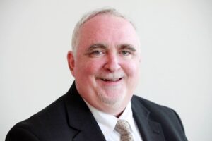 Head and shoulders shot of Jeff Flowers, smiling, wearing a dark suit and white collared shirt with a tie.