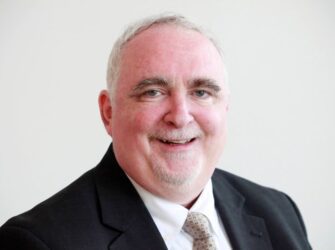 Head and shoulders shot of Jeff Flowers, smiling, wearing a dark suit and white collared shirt with a tie.