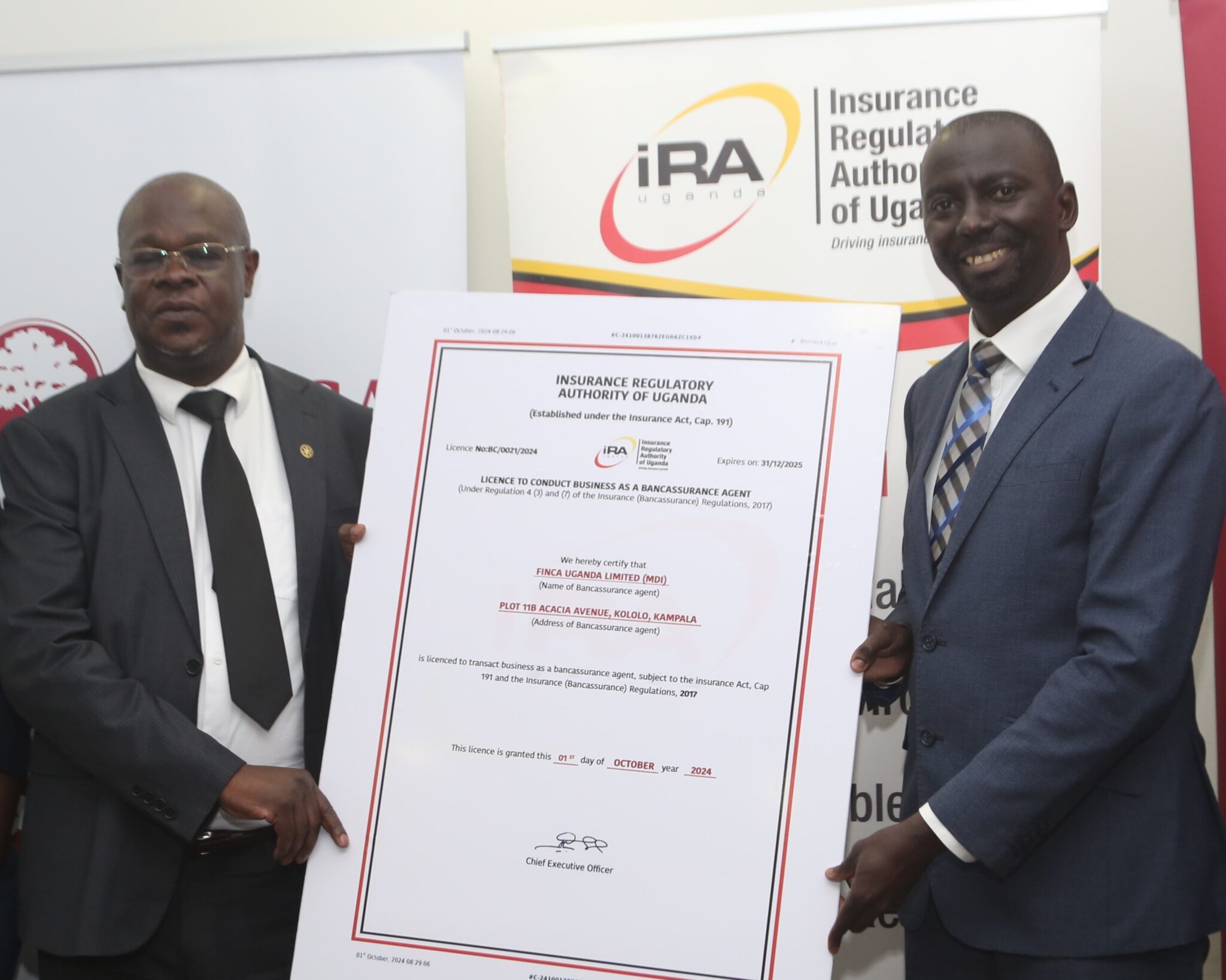 FINCA Uganda Managing Director James Onyutta and Benerd Obel, Director for Supervision, Insurance Regulatory Authority of Uganda hold poster-sized replica of FINCA Uganda's bancassurance license, which will enable FINCA to offer new insurance products to help customers protect their livelihoods and build resilience.