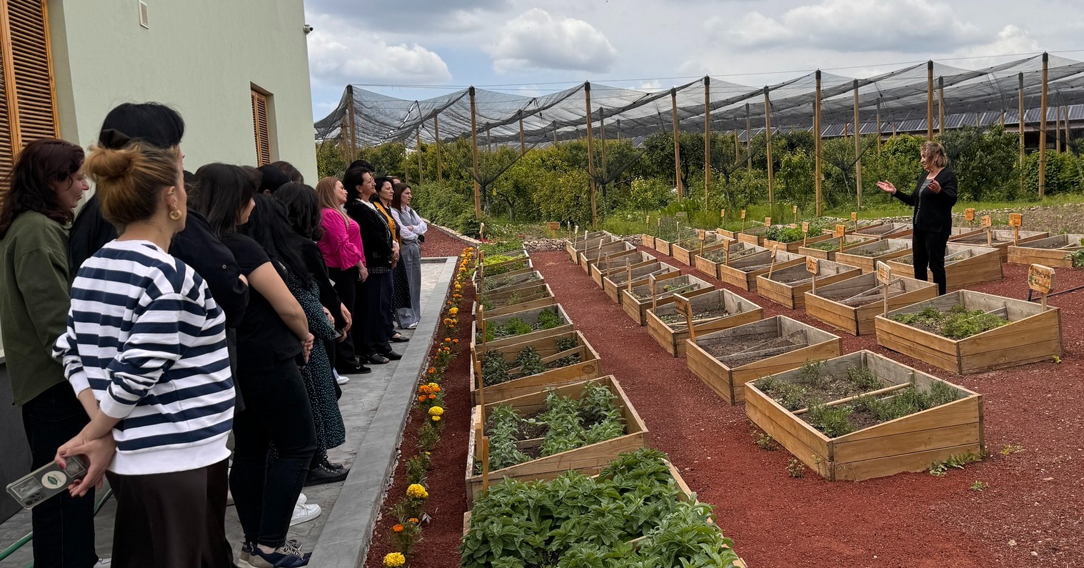 women standing behind rows of raised beds listening to an agriculture expert talk.